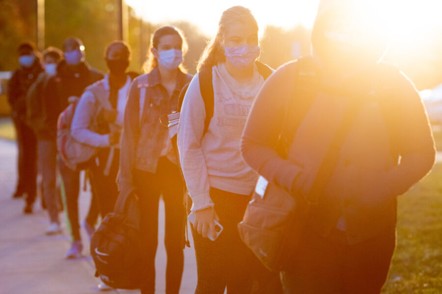 Students line up on socially distanced dots painted on the sidewalk to wait their turn to have their temperatures checked before entering Middletown High School.